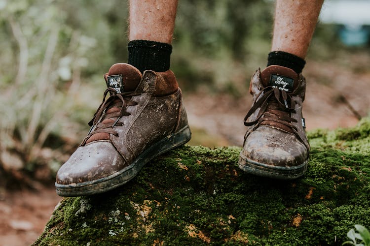 A Person Wearing Muddy Shoes While Standing On A Mossy Rock