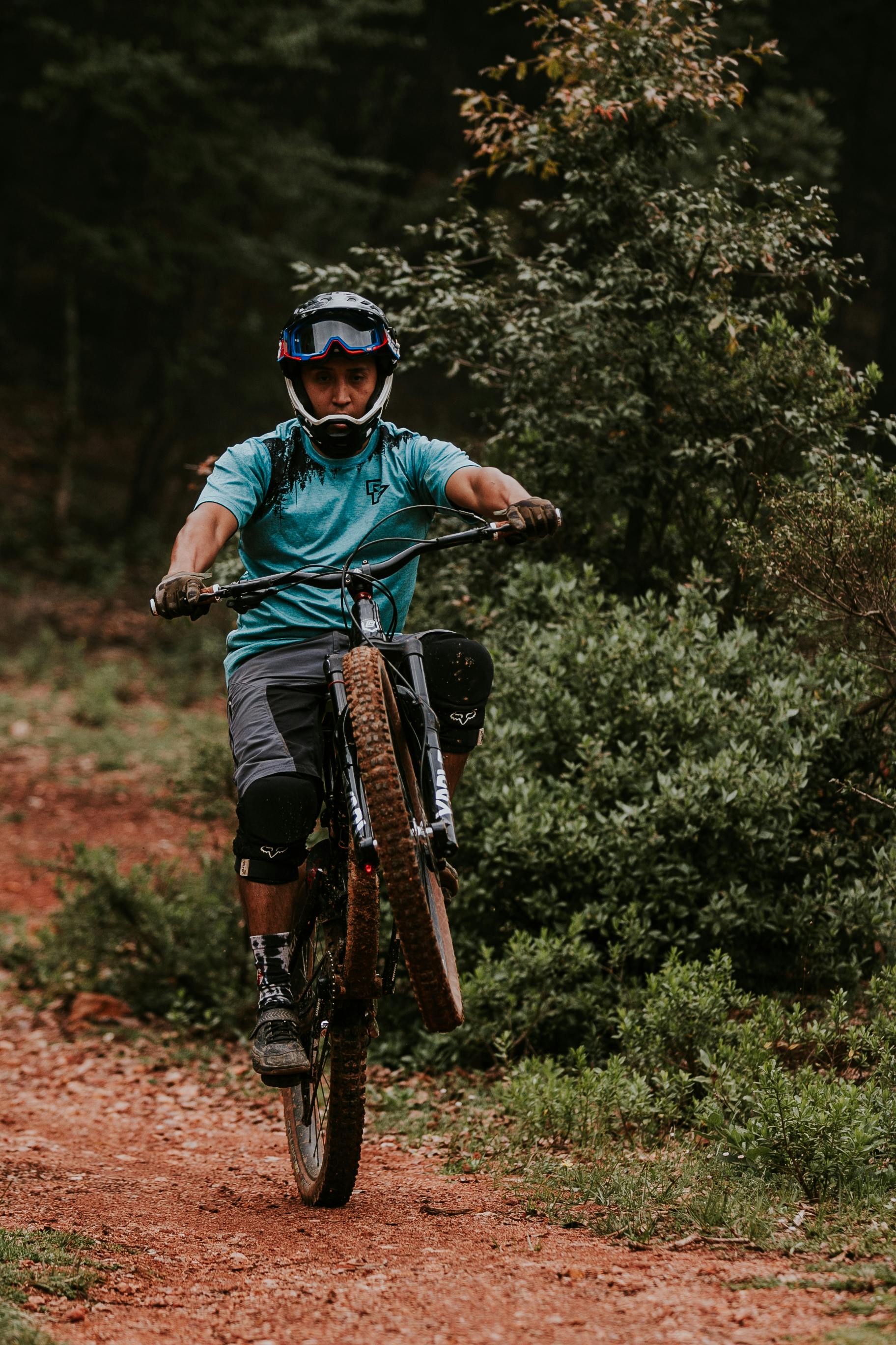 Mountain biker performs a wheelie on a forest dirt trail, showcasing outdoor adventure.