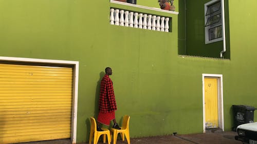 Woman Standing on Yellow Chairs Outside of Building with Green Walls