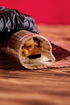A detailed view of a sushi roll being prepared on a bamboo mat with a vibrant red background.