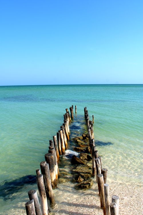 Free A serene view of turquoise waters and a weathered wooden breakwater on the shore of Chuburná, Mexico. Stock Photo