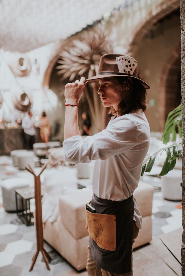 Man in White Long Sleeve Shirt with Apron and Hat Standing Near Tables