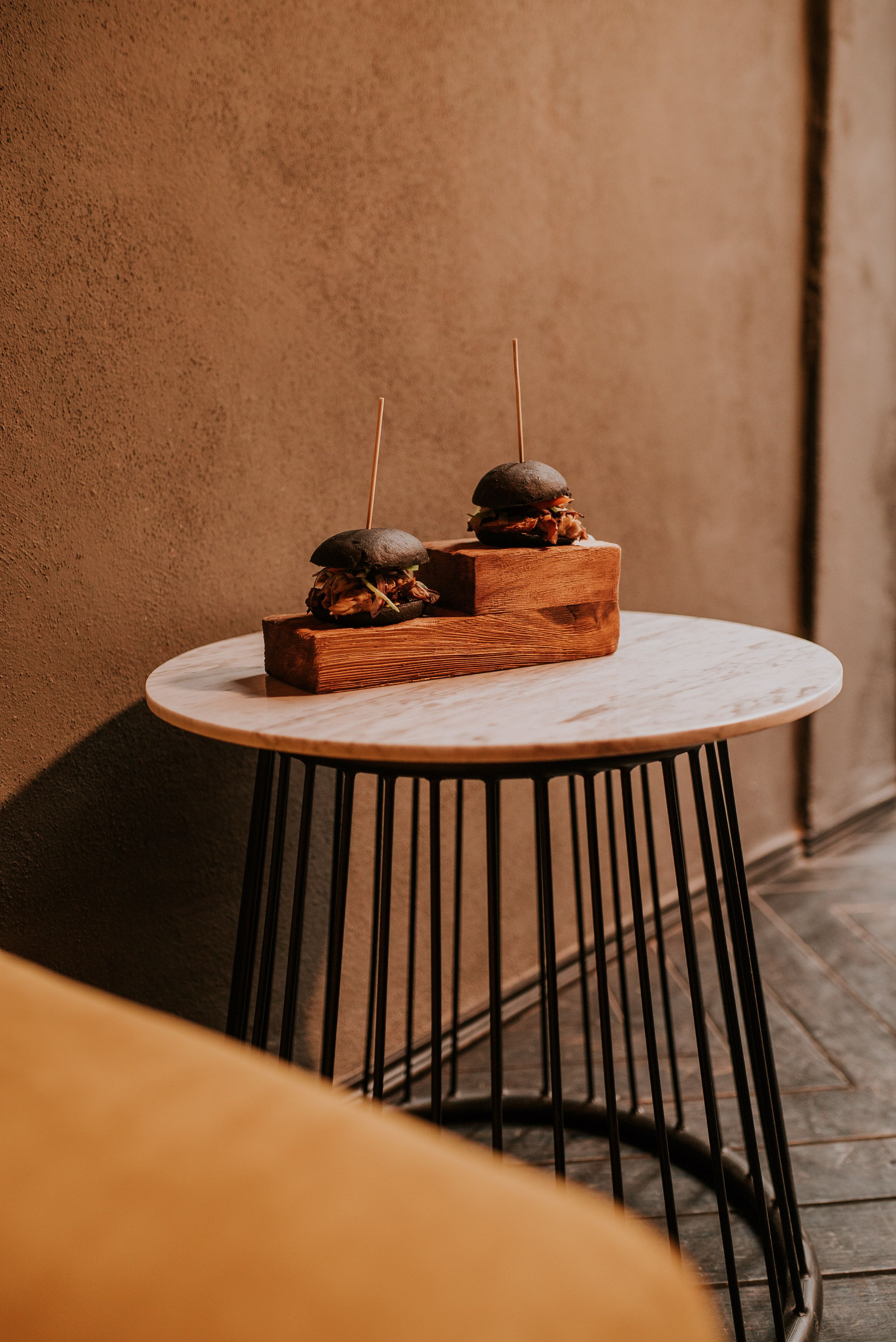 Elegant sliders with black buns served on a wooden board in a stylish restaurant setting.