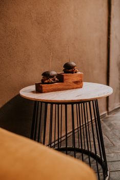 Elegant sliders with black buns served on a wooden board in a stylish restaurant setting.