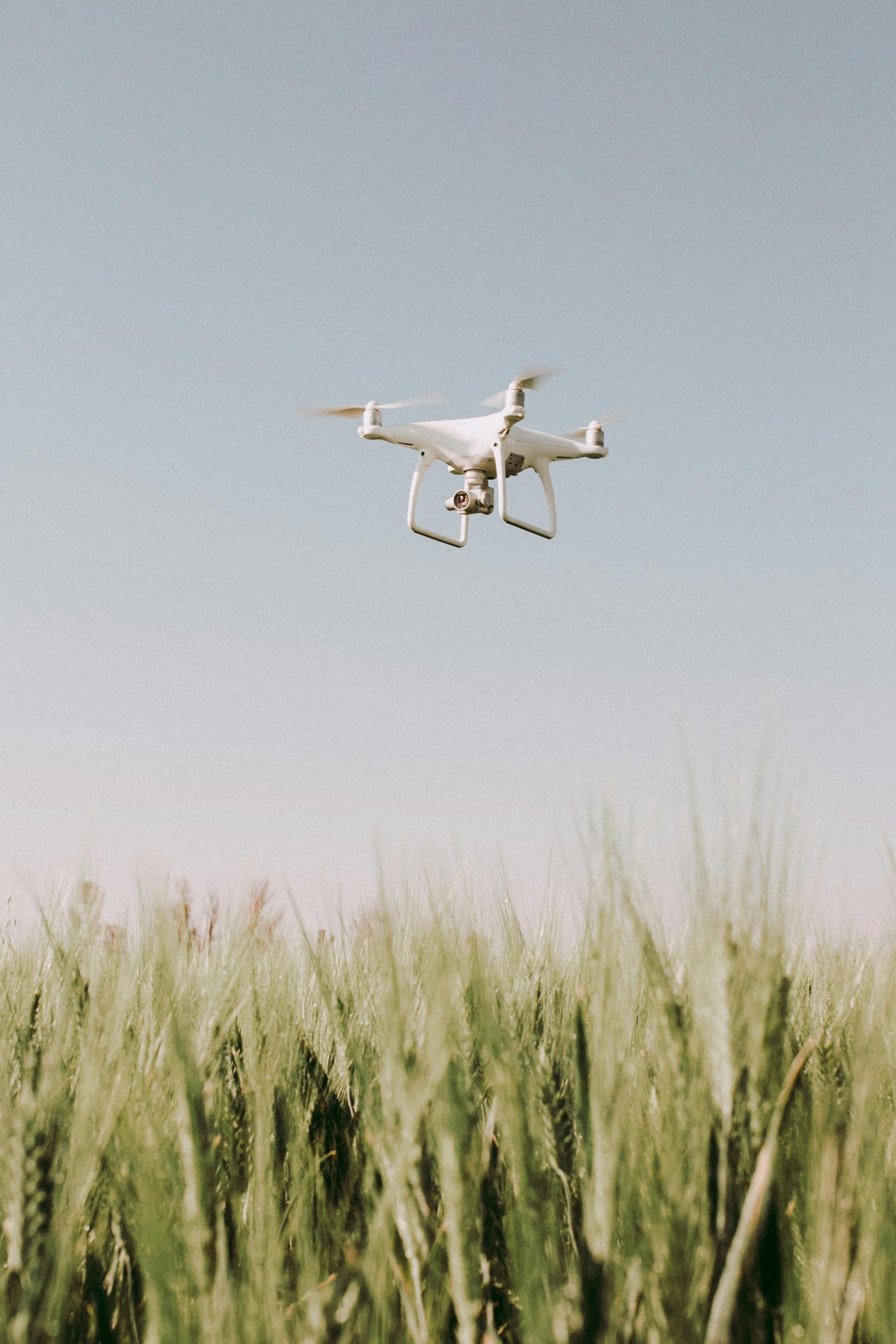 white drone flying over crop field