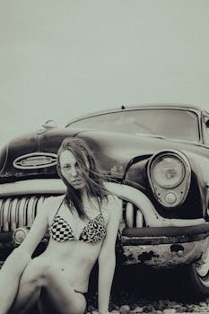 Young woman in bikini posing with a vintage car for a fashion photoshoot, creating a retro aesthetic.