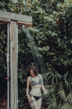 A woman enjoys a refreshing outdoor shower surrounded by lush greenery in a tropical setting.