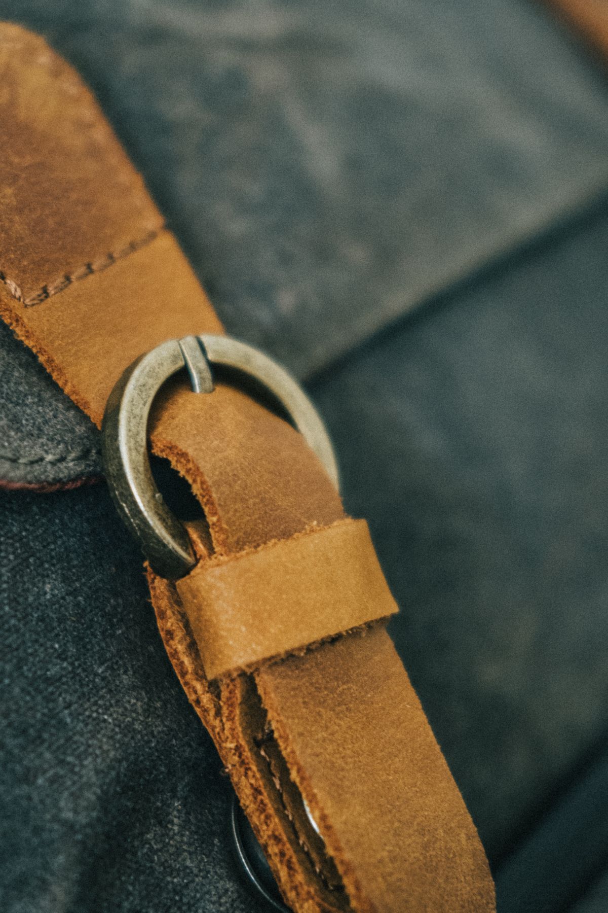 Close-up of a metal buckle on a tan leather strap stitched to a waxed canvas bag