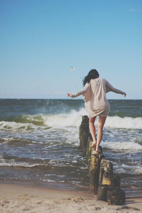 Woman Wearing Brown Long-sleeved Dress Stepping on Brown Pillar Stands