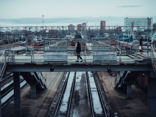 Free Aerial view of a footbridge over railway tracks in an urban setting with a person walking. Stock Photo