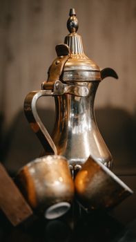 Metal coffee pot with cups on a reflective surface, showcasing an elegant still life arrangement.