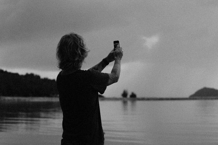 A Person Taking A Photo With A Smartphone While Standing By A Lake 