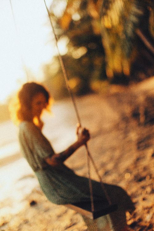 Free A woman sitting on a swing by the beach during a soft golden sunset, captured with a dreamy focus. Stock Photo
