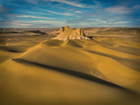 Explore the vast golden dunes and rock formations of Kumtag Desert under a brilliant blue sky.