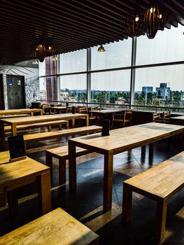Wooden tables and benches in a Bengaluru rooftop cafe offering a view of the city.
