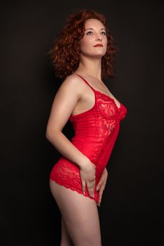 A caucasian woman in red lingerie poses against a dark background, exuding elegance and confidence.