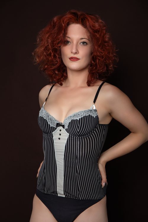 Free Redheaded woman posing in monochrome lingerie against a dark background in a studio setting. Stock Photo