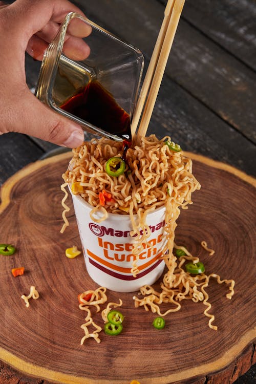 Person Pouring Soy Sauce on Noodles