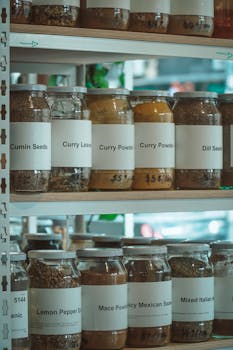 Close-up shot of various spices in labeled glass jars on wooden shelves in a store.