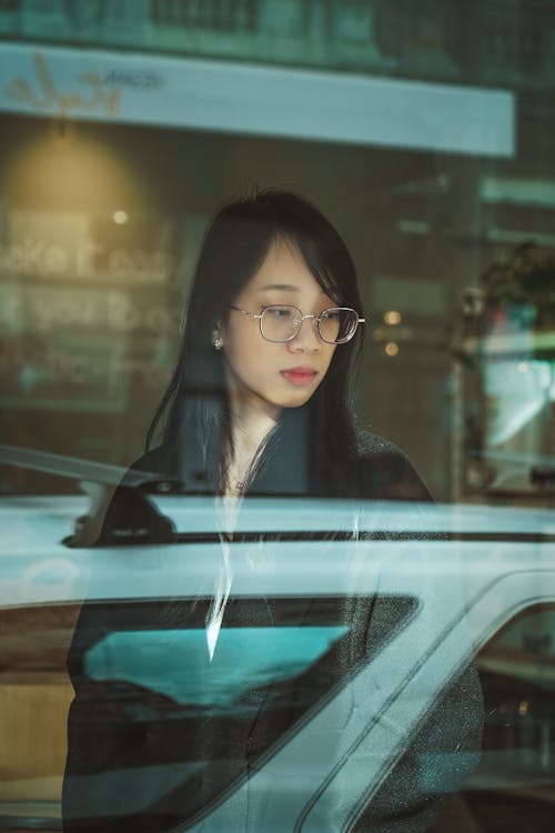 Woman in Black Coat Standing Beside Glass Window