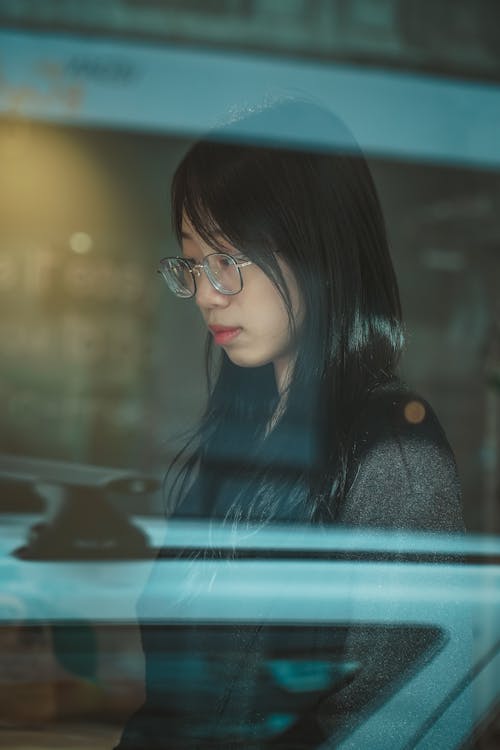 Woman in Black Coat Standing Beside Glass Window