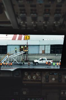 View from airplane cockpit of ground crew preparing for aircraft maintenance at airport.