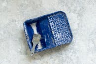 Dark blue painting tray with a little white paint and an old rusty brush lying on the dusty concrete floor in a renovated room in apartment or house