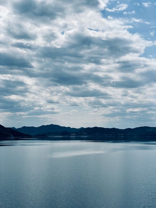 Free Serene view of a calm lake with distant mountains and a cloudy sky. Stock Photo