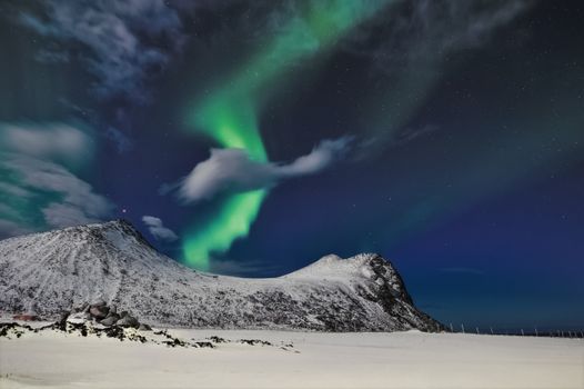 Beautiful aurora borealis illuminating snowy mountains in Myrland, Norway, under a starry night sky.