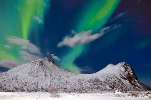 Majestic aurora borealis lighting up the night sky over snow-covered mountains in Myrland, Norway.