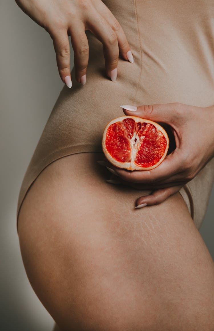 Woman Holding A Red Orange Next To Her Hip