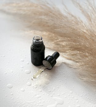 Close-up of a skincare bottle and dropper with pampas grass and water droplets for a fresh feel.