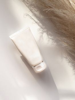 Elegant white cosmetic tube with shadows on a neutral background, suitable for beauty product presentations.