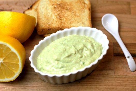 Delicious avocado spread in a white dish, accompanied by lemon and toast.