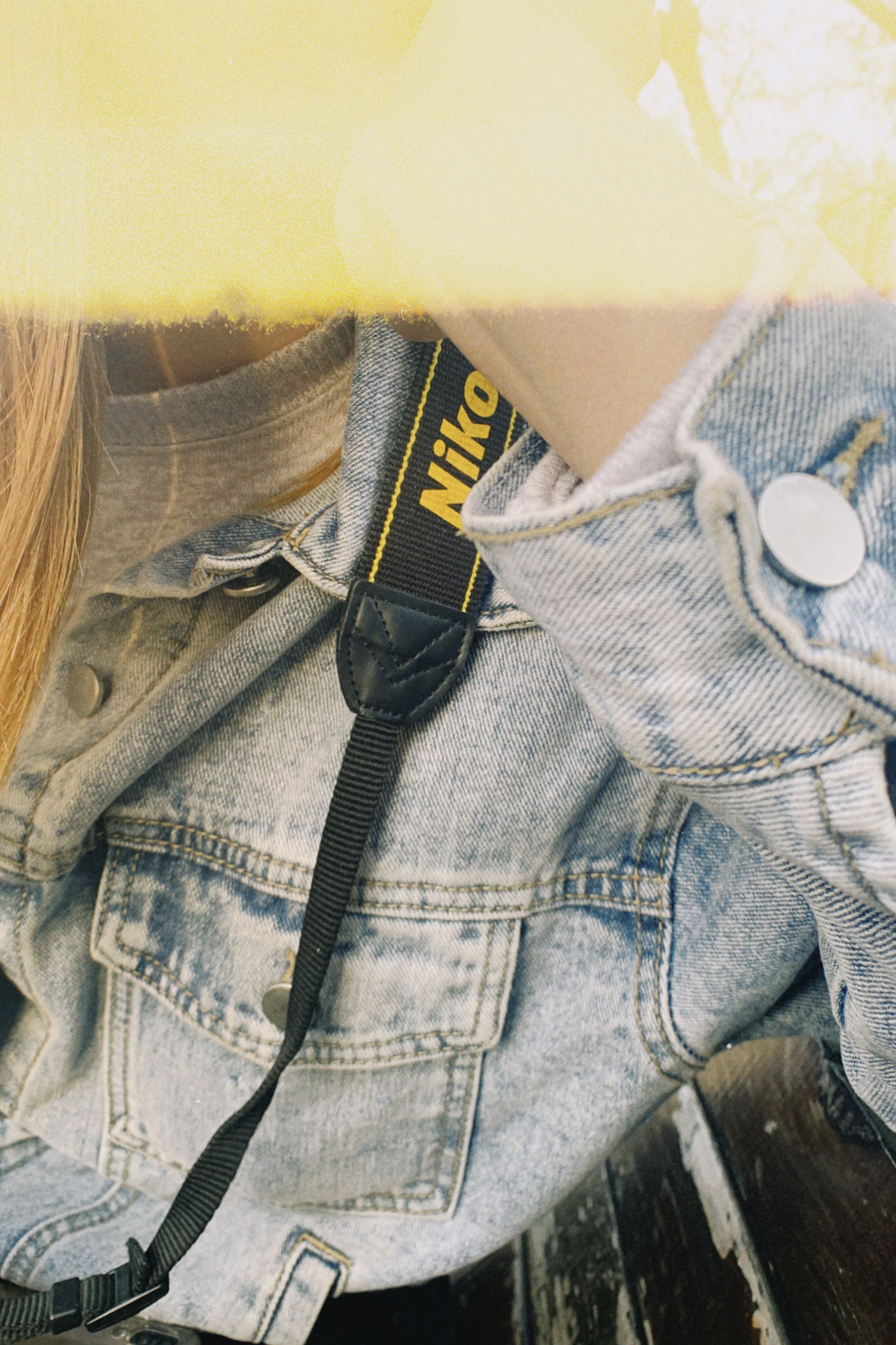 Close-up of a denim jacket with a camera strap, emphasizing casual fashion and photography gear.