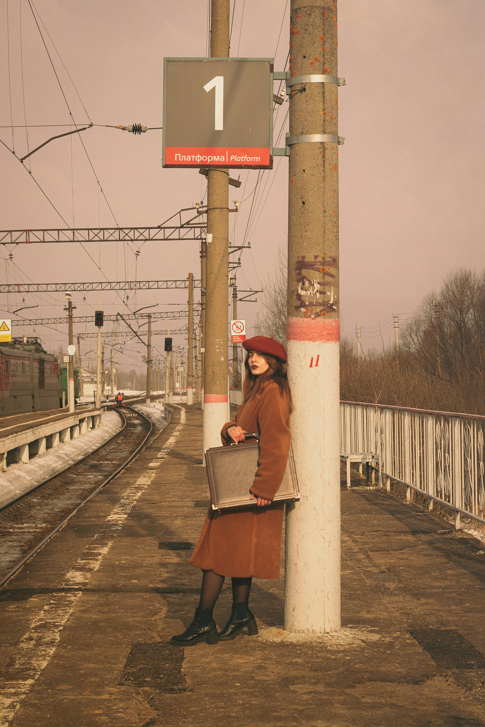 A stylish woman in a beret waits at a Moscow train station platform, evoking a sense of travel and adventure.