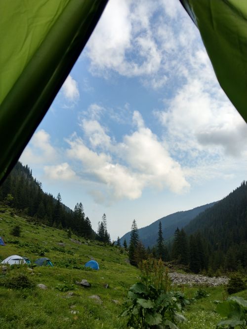 Free A serene camping scene with tents in a lush mountain valley under a blue sky. Stock Photo