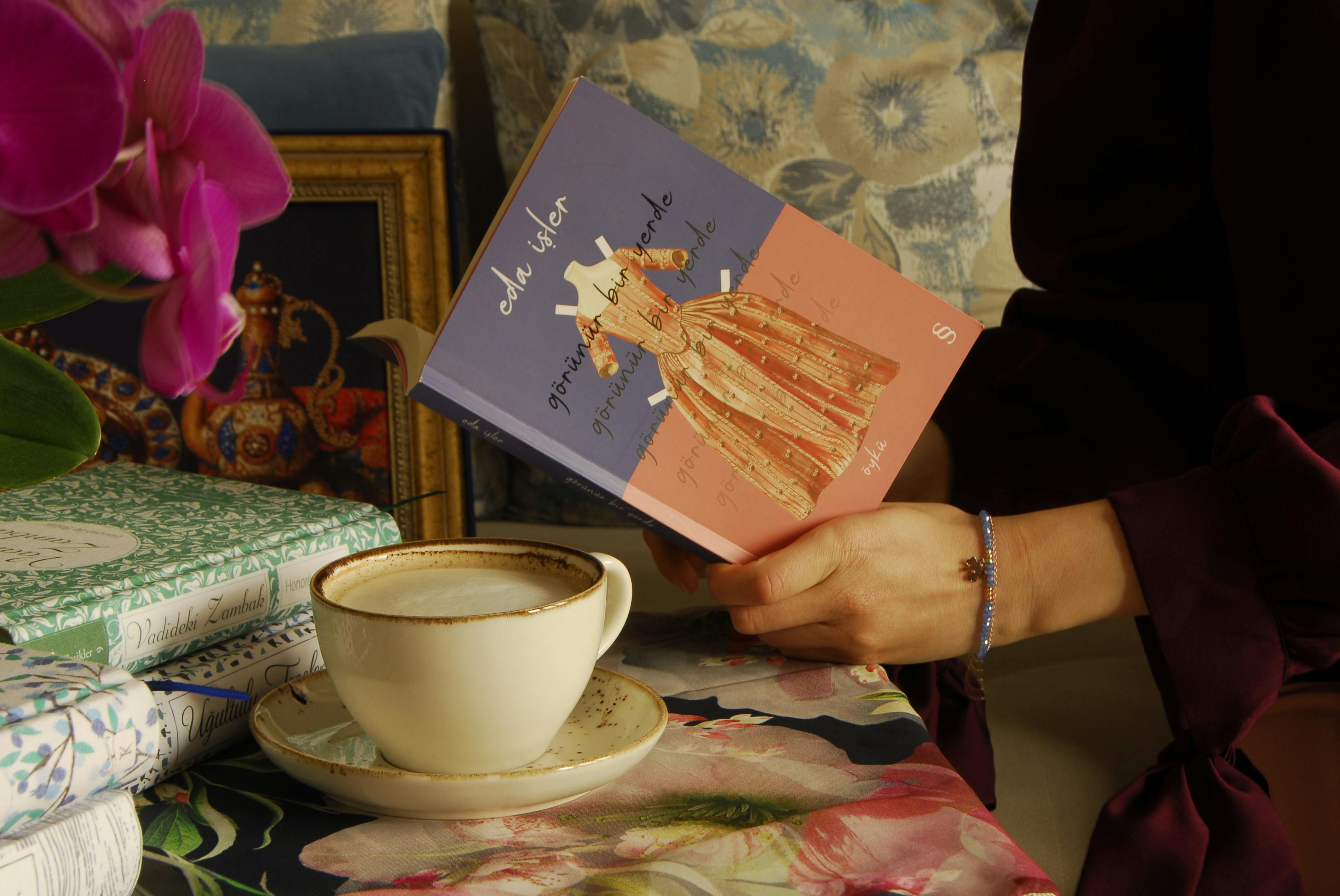 A serene scene of holding a book with a cup of coffee on a florally decorated table.
