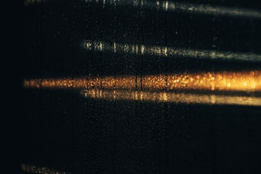 Close-up of a glass window with water droplets and blurred lights reflecting during nighttime.