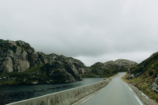 Discover the serene beauty of a winding mountain road amidst Norway's rugged terrain and cloudy skies.