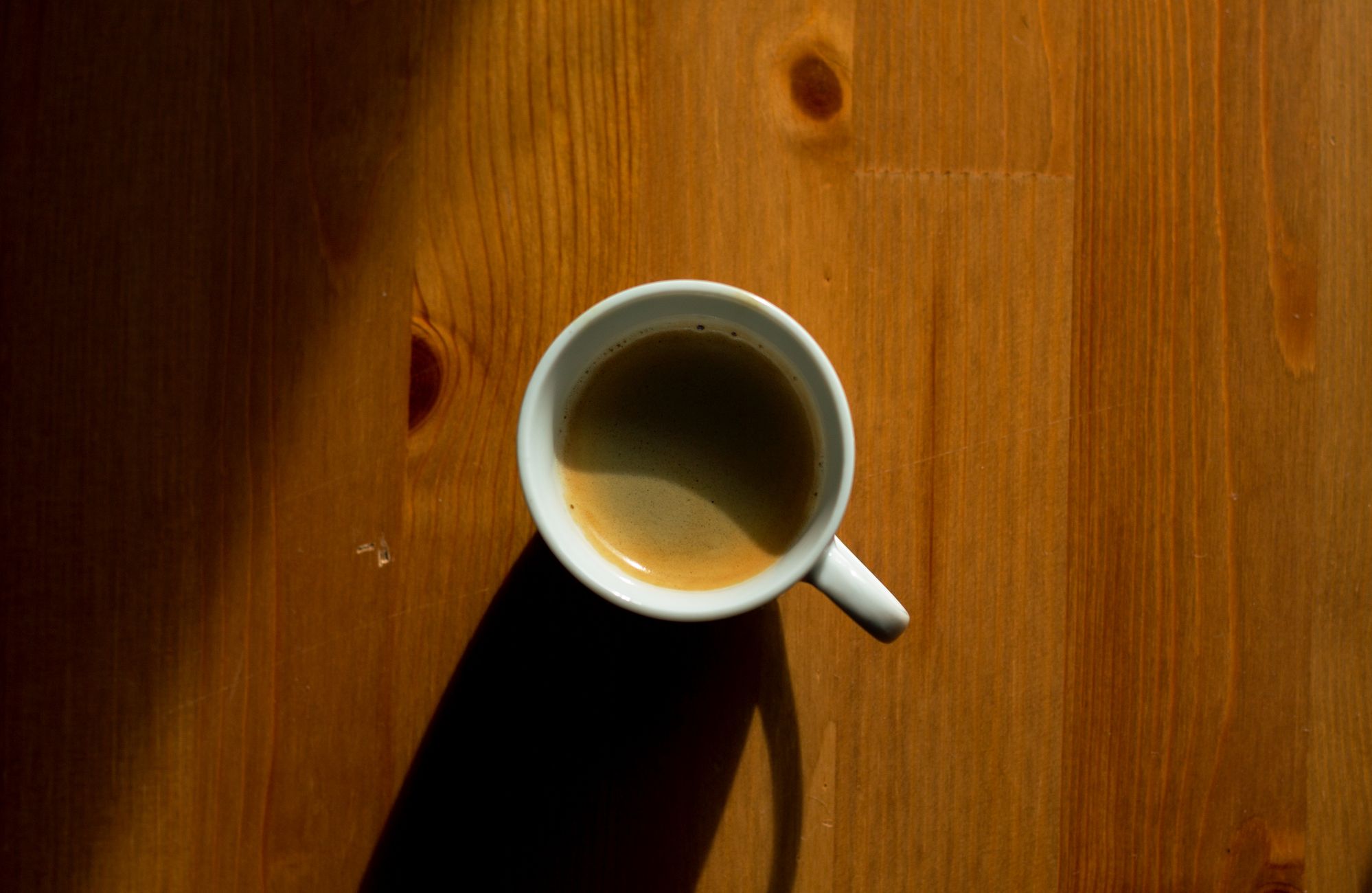 A simple, minimalist approach capturing a cup of coffee casting a shadow on a wooden table.