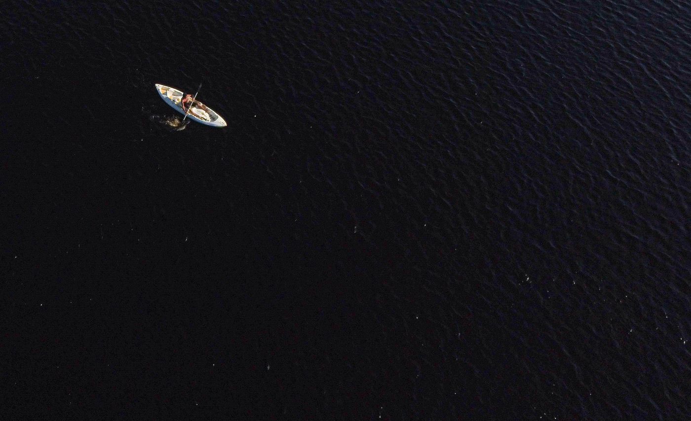A lone canoe on dark lake water seen from above, photo by Zeca Souza on Pexels