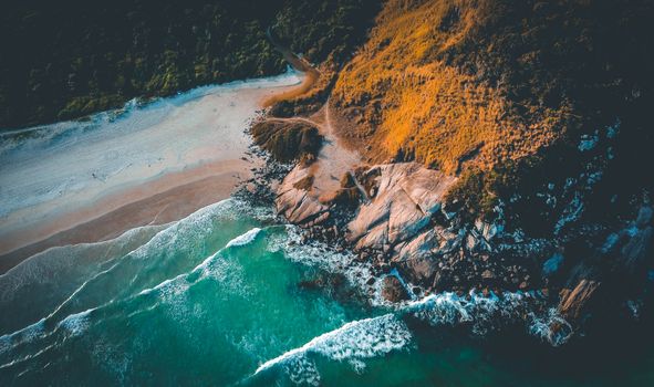 Stunning aerial shot of a scenic rocky coastline with vibrant green waves crashing onto the shore.