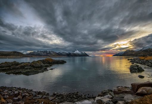 A captivating sunset over a serene lake in Napp, Nordland, Norway, framed by rugged mountains.