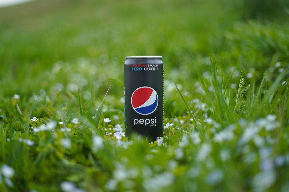 Close-up of a Pepsi Max can surrounded by lush green grass and small flowers.