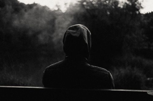 Free A person in a hoodie sits alone outdoors, captured in black-and-white, creating a moody and contemplative atmosphere. Stock Photo
