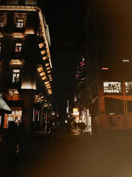 Explore the lively urban street of Greece illuminated in nighttime ambiance with people walking.