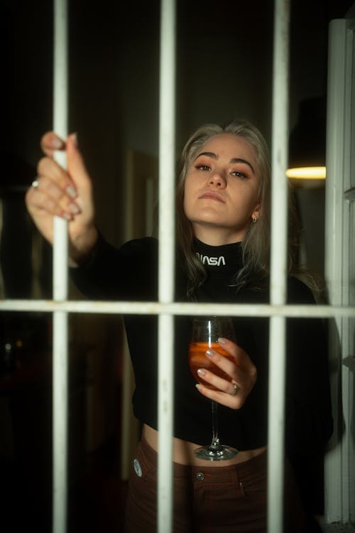 Woman Holding Cocktail in Her Hand and Leaning Against a Steel Gate