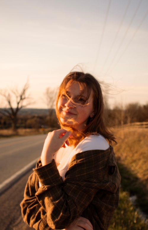 Free A woman smiles warmly on a country road at sunset, embodying joy and freedom. Stock Photo