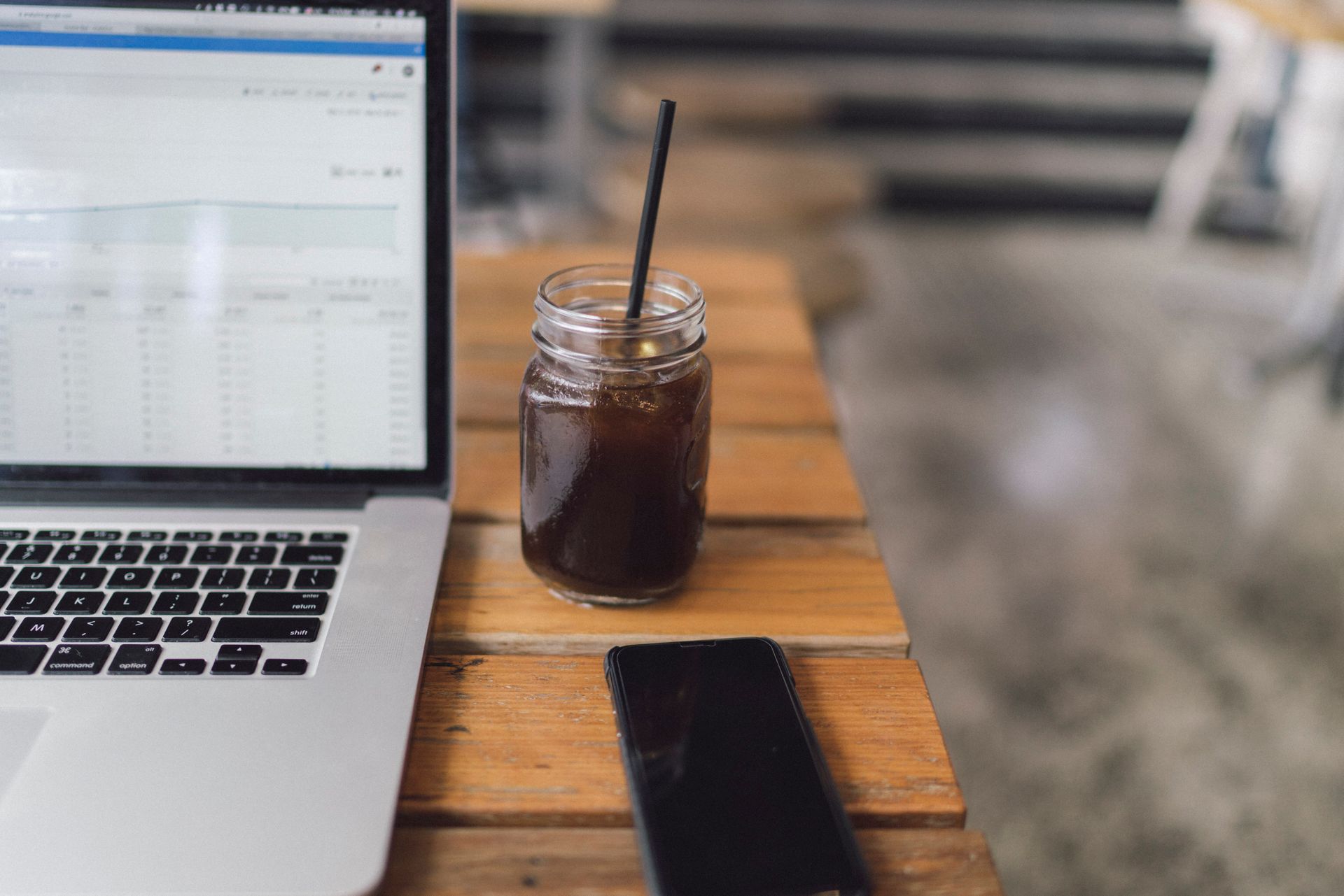 A cozy workspace featuring a laptop, coffee in a mason jar, and a smartphone on a wooden table.